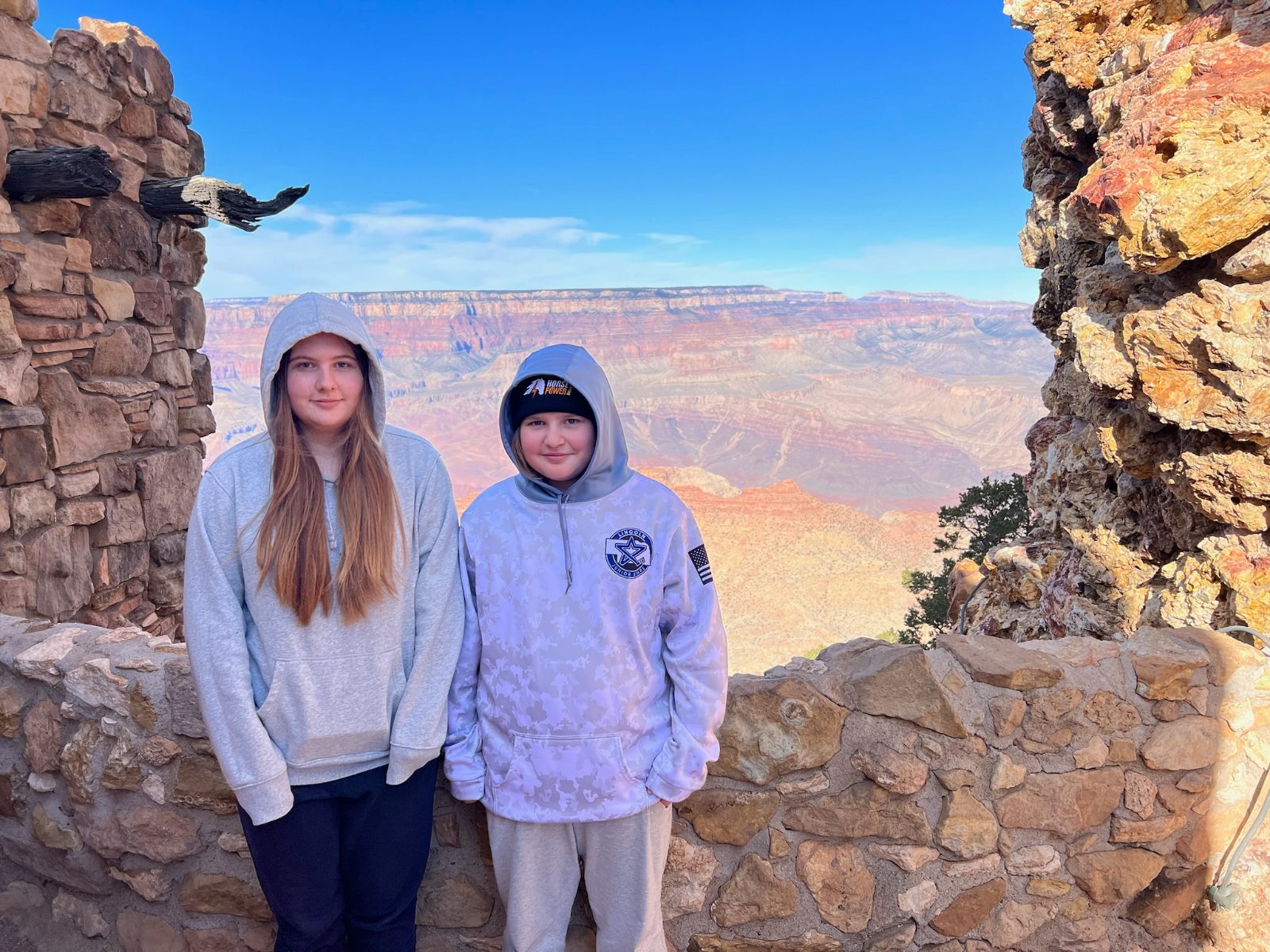 Lily and Landon standing between the rough stone walls of the Desert View Watchtower, the canyon behind them