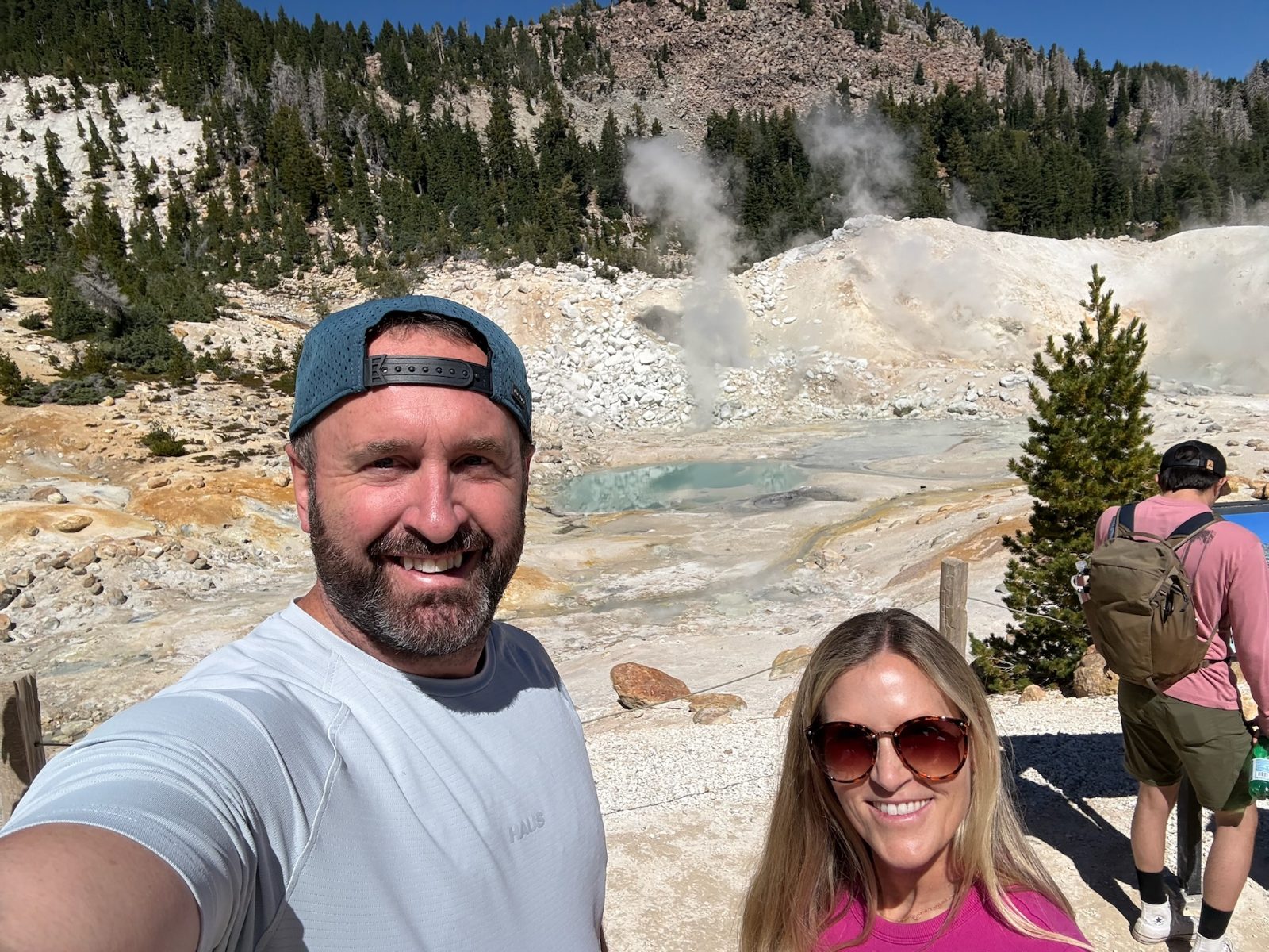 Tony and Trisha in the Bumpass Hell basin, a steaming turquoise pool and white mineral ground behind them