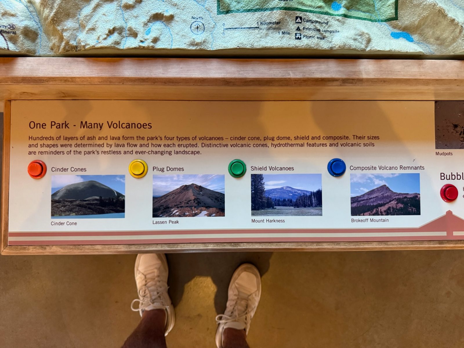 A visitor center exhibit titled One Park, Many Volcanoes with four buttons and photographs labelled Cinder Cone, Lassen Peak, Mount Harkness and Brokeoff Mountain