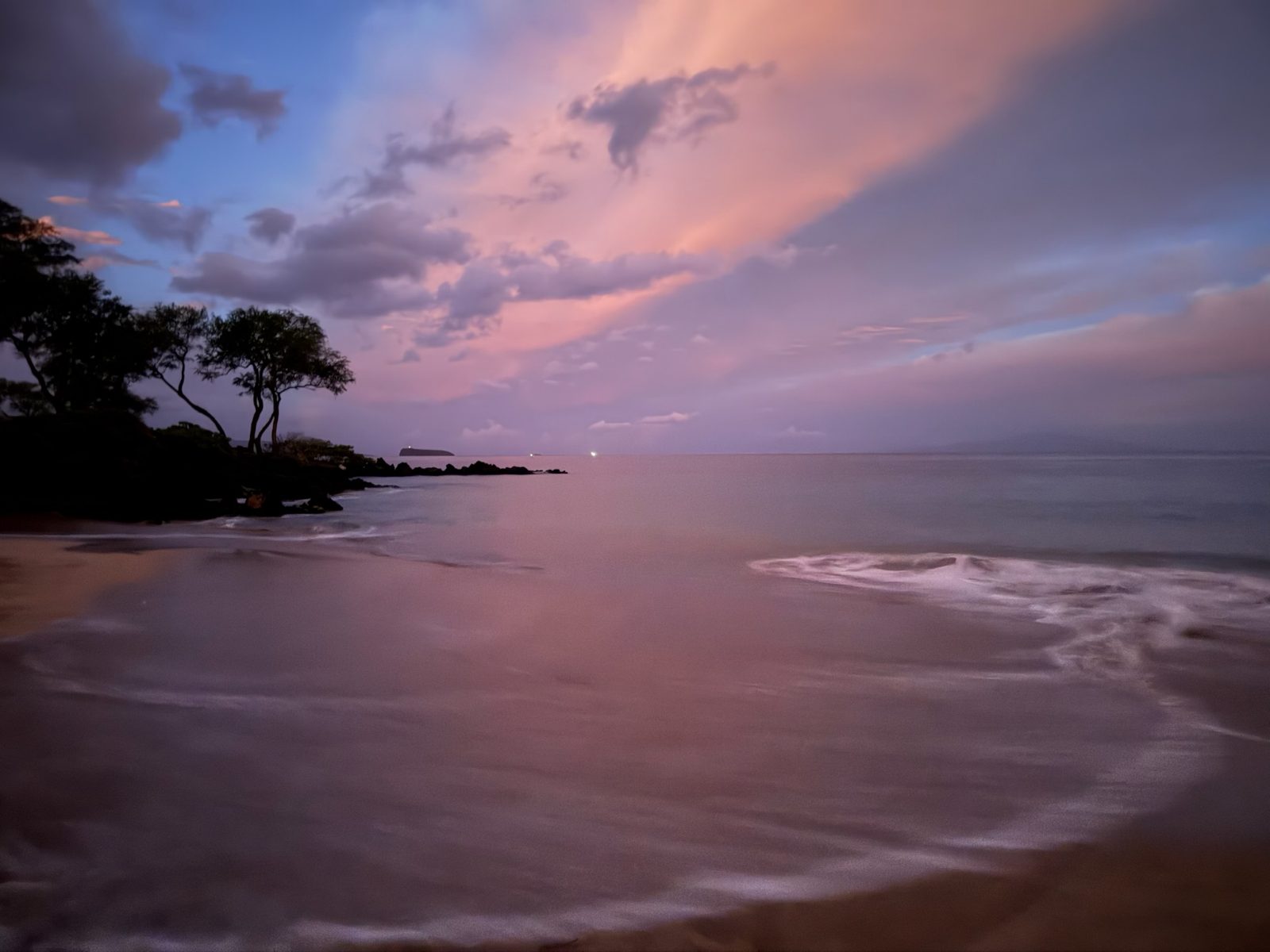 Dawn over the water on the south-west coast of Maui, pink and purple cloud over a long exposure of the surf, with islands silhouetted on the horizon